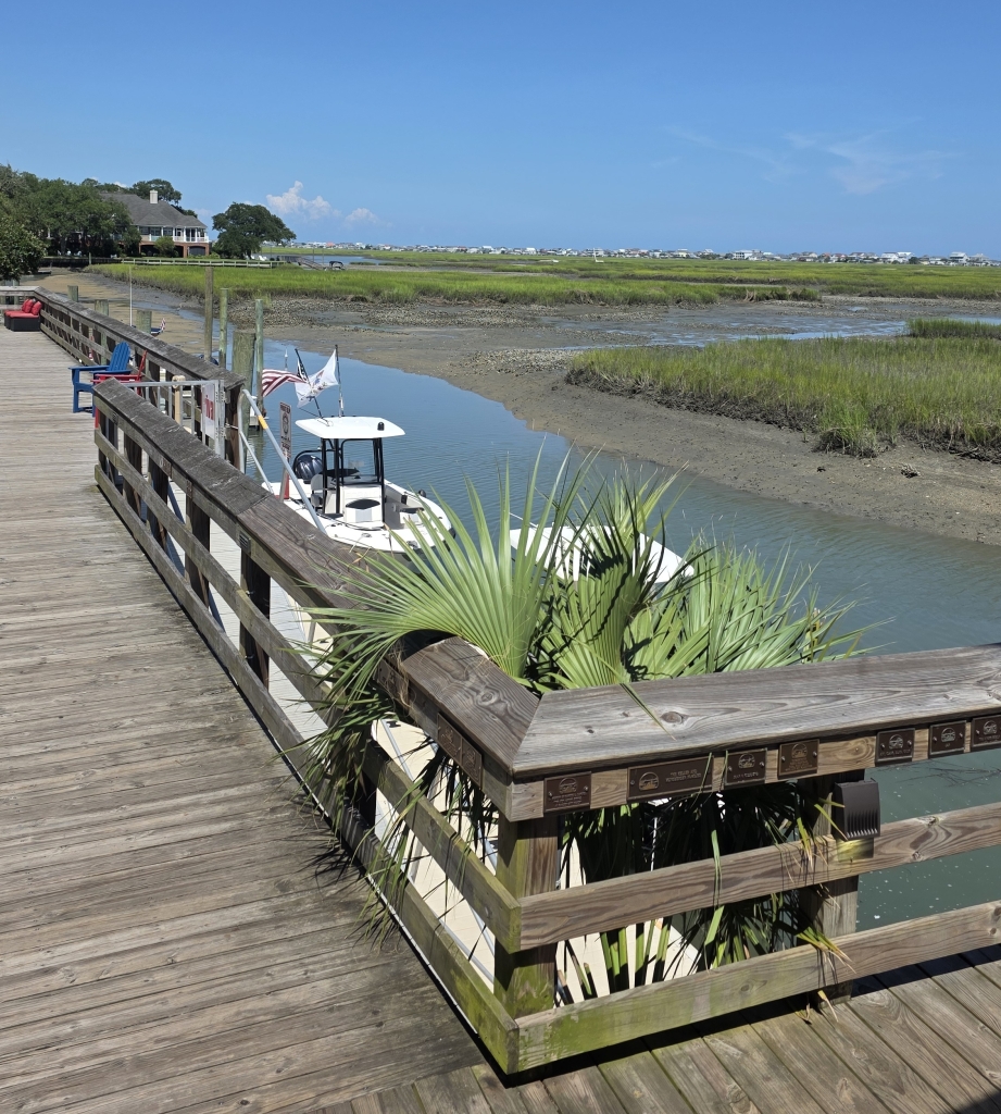 Daytime view of the Murrells Inlet MarshWalk with boats and marsh grass in Murrells Inlet, SC.