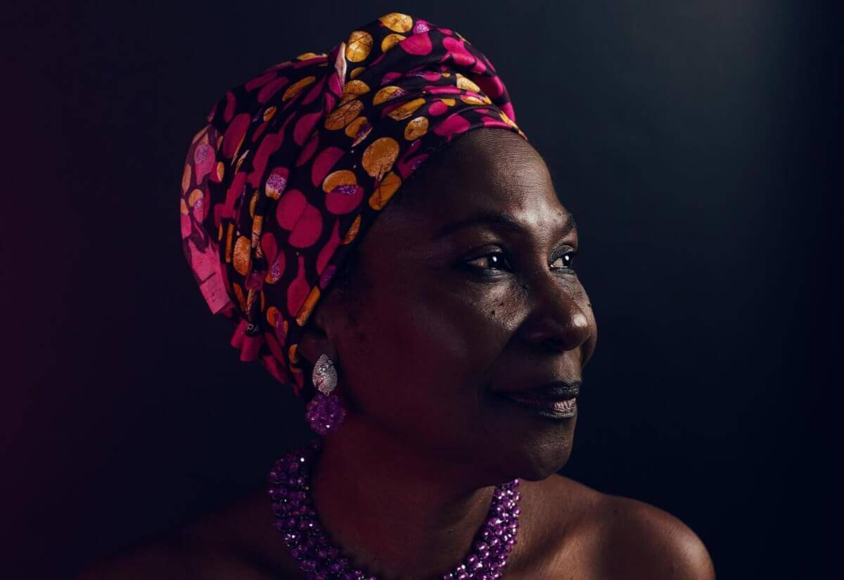 Portrait of a woman wearing a colorful patterned headwrap and beaded jewelry, symbolizing the pride and strength of Gullah Geechee culture.