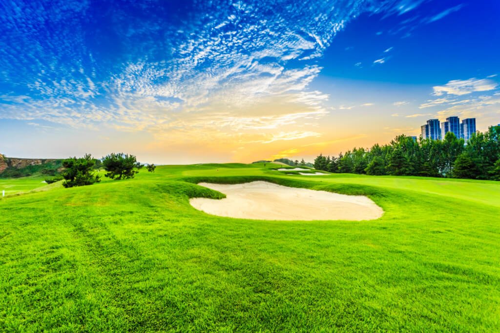 A serene golf course with lush green grass and shimmering water reflecting the vibrant colors of a breathtaking sunset.