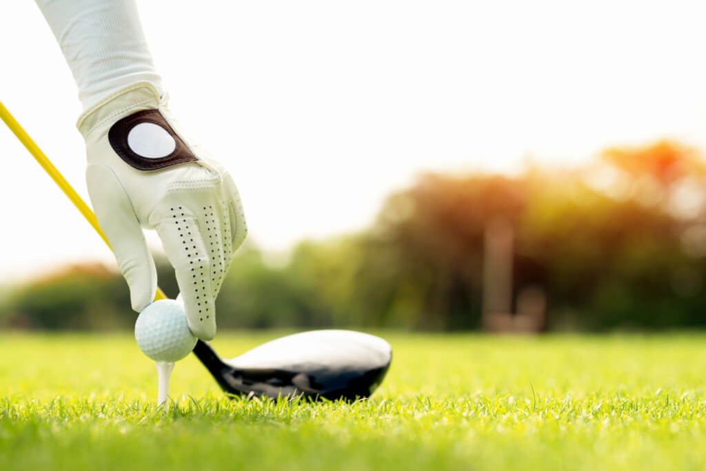 A golfer teeing a golf ball on a grassy field.