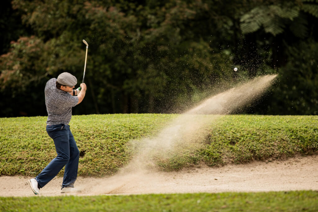 A golfer skillfully swings a club, hitting a golf ball out of a sand bunker on the course.