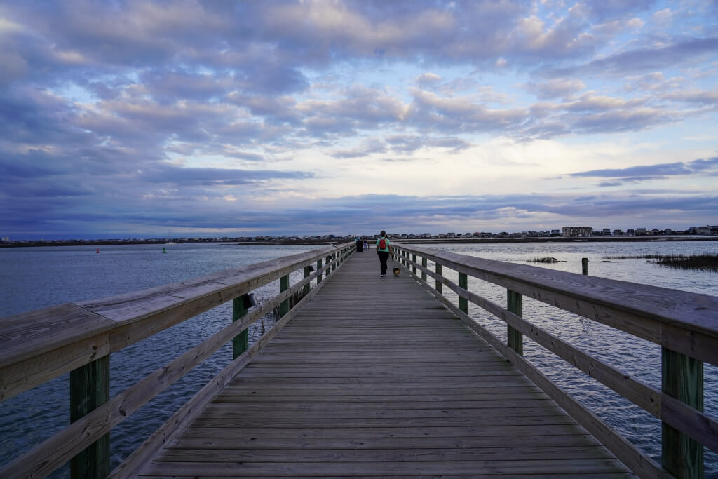 Scenic view of the Murrells Inlet MarshWalk boardwalk at sunset with people and a dog enjoying the waterfront.