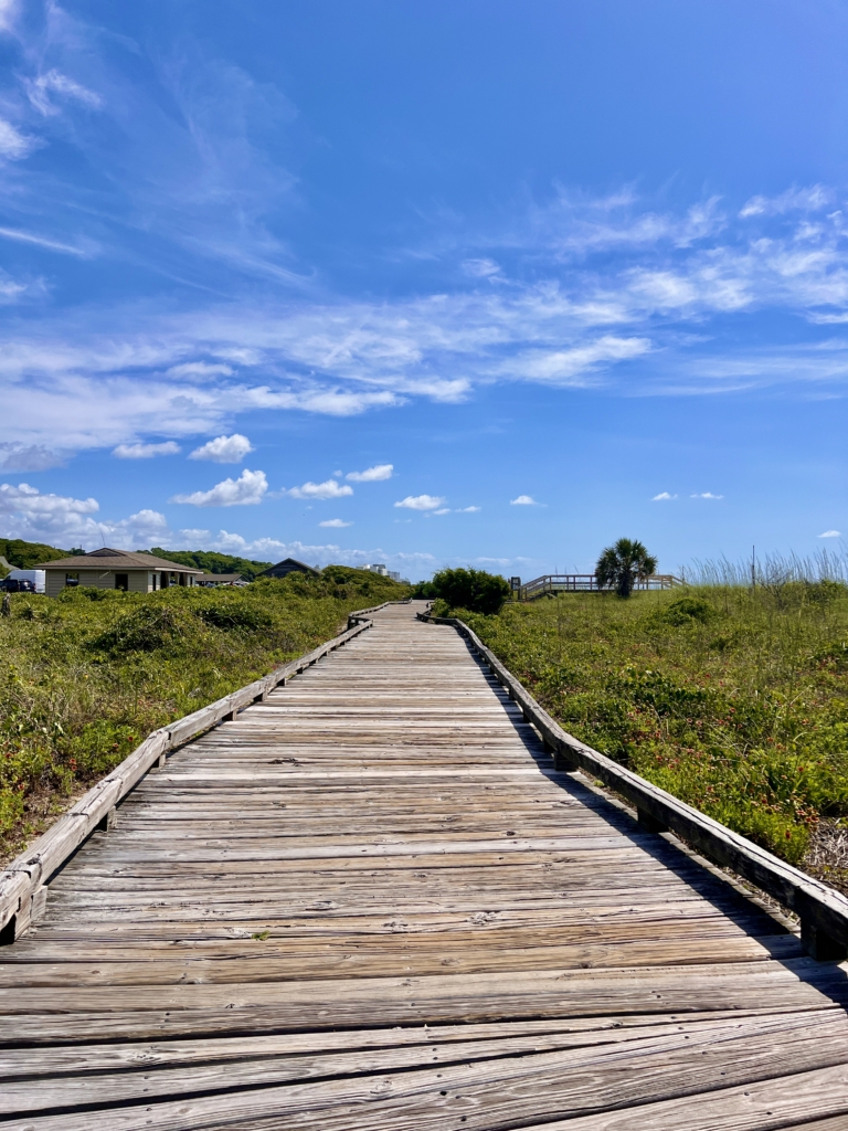 Sunny boardwalk trail leading through grassy dunes at Myrtle Beach State Park.