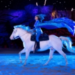 A person rides a white horse in blue lighting at Dolly Parton's Stampede in Pigeon Forge, TN.