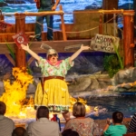 A woman in goggles holds her arms up in front of a pond on fire at Hatfield & McCoys Dinner Feud in Pigeon Forge, TN.