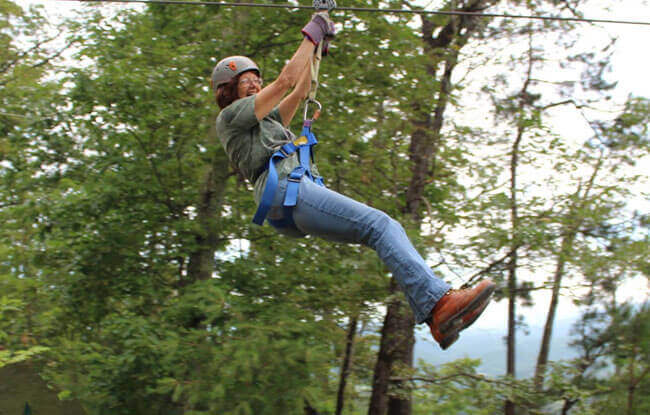 Woman enjoying a solo zipline ride through the trees at Legacy Mountain near Gatlinburg.
