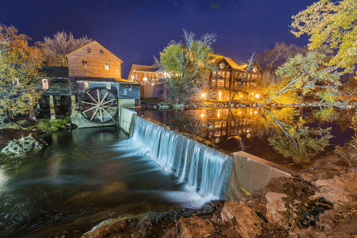 A picturesque water wheel and mill illuminated under the Pigeon Forge night sky, creating a serene and enchanting scene.