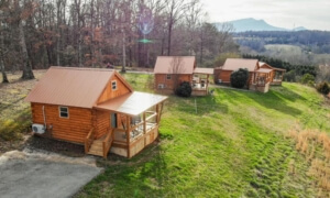 A cabin nestled among lush trees and towering mountains.